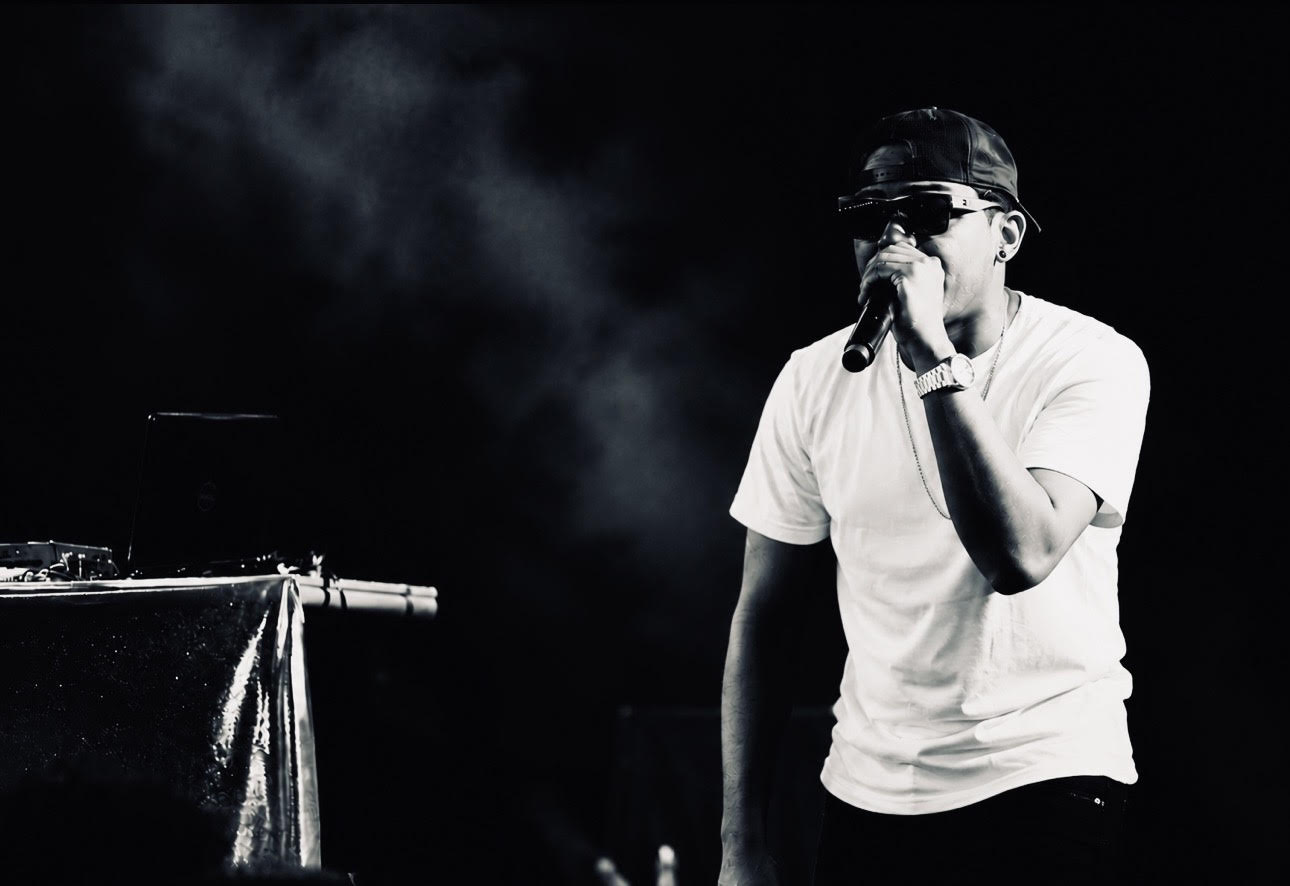Thello Jay performing live on stage, holding a microphone amid stage haze